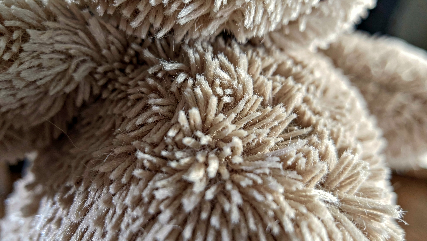 Ein einzelner brauner Teddybär liegt auf einem ordentlich gefalteten Stapel Kinderkleidung neben einer kleinen Reisetasche auf einem Holzboden, weiches Morgenlicht von links, Nahaufnahme aus leichter Aufsicht.