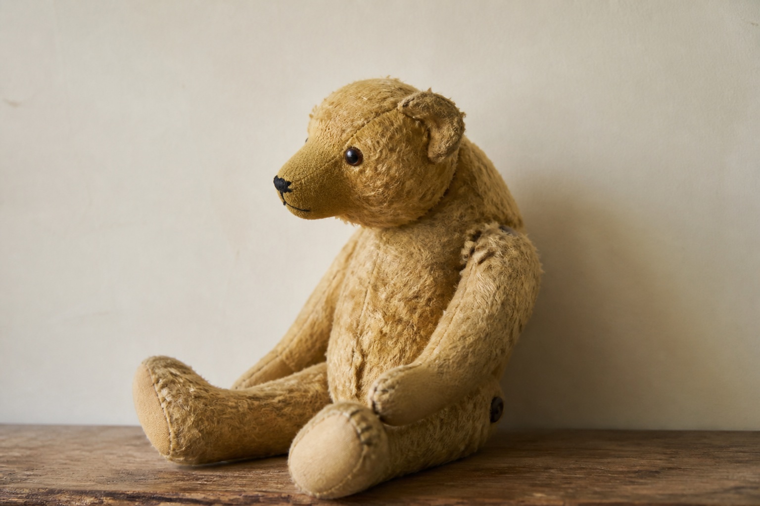Ein Holztisch am Fenster mit einer geöffneten Schachtel alter Schwarzweißfotos, daneben ein abgegriffener Teddybär mit fehlendem Auge, weiches Seitenlicht von links, Nahaufnahme aus leichter Aufsicht.